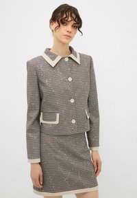 Giacca in tweed a quadri marrone e crema con ampio colletto, chiusura a bottoni, due tasche frontali e gonna aderente coordinata.