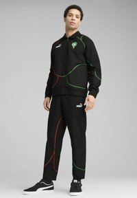 Chándal negro que incluye una chaqueta con cremallera con patrones de líneas verdes y rojas, combinado con pantalones a juego. Incluye el logo de Puma en el pecho y en los pantalones.