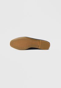 Black shoe sole with a smooth, rubberized finish and textured gripping pattern. Features a beige edge and logo imprint on the sole.