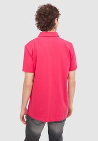Polo de manga corta en algodón de color rosa brillante. Presenta un collar clásico y un dobladillo recto. Diseño sencillo sin acentos o patrones adicionales.