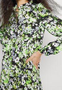 Floral dress in green, black, and white, featuring long sleeves, a ruffled collar, and side pockets with a loose fit and pleated design.