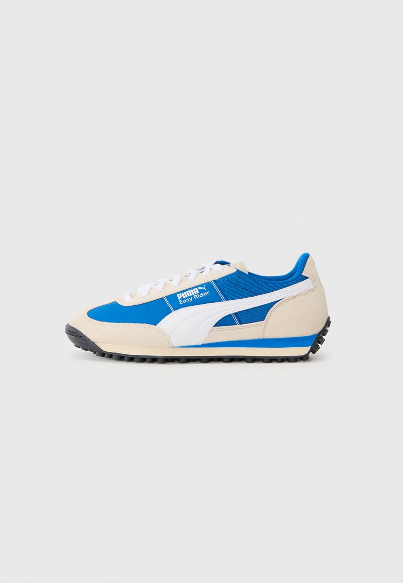 Sneaker blu e beige realizzato con materiali in camoscio e rete, caratterizzato da una striscia bianca, chiusura con lacci e suola in gomma nera testurizzata.