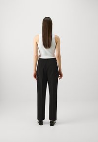 Pantalon noir ajusté à coupe droite, avec une taille, des détails de poche au dos, associé à un débardeur blanc à côtes. Texture de tissu lisse.