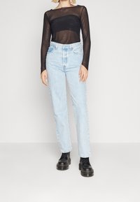 Svart mesh långärmad topp med prickig textur, kombinerad med ljusblå högmidjade jeans och svarta snörkängor.