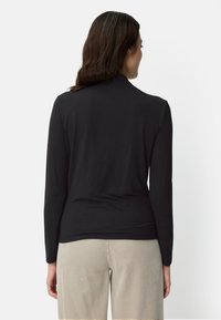 Czarna bluzka z długim rękawem wykonana z gładkiej tkaniny, o prostym kroju i wysokim dekolcie. Noszona z beżowymi, teksturowanymi spodniami.