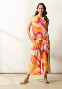 Top bez rękawów i szerokie spodnie w kolorowy falisty wzór z odcieniami różu, czerwieni, pomarańczy i żółci. Wykonane z lekkiej, gładkiej tkaniny.