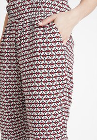 Röda och svarta mönstrade byxor med en blomstergeometrisk design, elastisk midja och sidofickor. Slät, lättviktsmaterial.