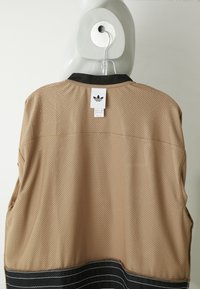 Μπεζ αεροδιάτρητο αθλητικό μπλουζάκι Adidas με μαύρο γιακά και κάτω άκρη, κρεμασμένο σε άσπρο μανεκέν σε απλό ανοιχτό φόντο.