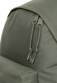 Mochila verde oliva confeccionada con tela duradera, con parte superior redondeada, superficie texturizada y dos tiradores de cremallera grises con cordones anudados.