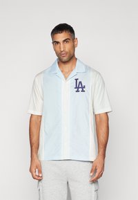 Hemd mit kurzen Ärmeln in einem hellblauen und weißen Farbblockdesign. Verfügt über ein gesticktes LA-Logo auf der Brust und eine Knopfverschluss.