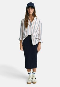 Camicetta a righe con maniche arrotolate, maxi gonna in maglia blu scuro, sneakers bianche con suole marroni e cappellino blu.