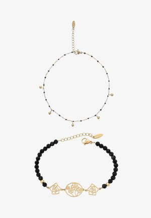 Dwie bransoletki w kolorze złota i czerni: jedna cienki łańcuszek z małymi złotymi zawieszkami, druga z koralików z złotymi kwiatowymi i geometrycznymi zawieszkami.