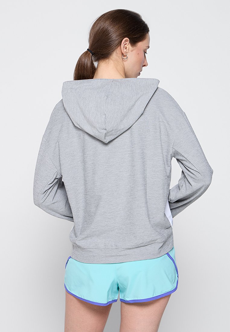 Sudadera ligera gris con capucha ajustable, presenta mangas largas y tejido texturizado, combinada con pantalones cortos turquesa con ribetes morados.