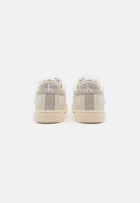 Sneakers Calvin Klein in pelle beige chiaro con accenti bianchi. Forma arrotondata, profilo basso e dettagli testurizzati sul tallone.