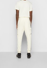 Cream cargo pants with black side stripe, elastic cuffs, and pockets. Paired with a light-colored t-shirt and black sneakers.