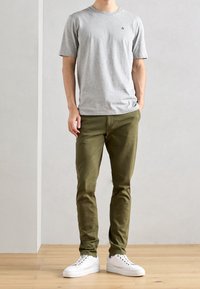Grijze katoenen t-shirt met ronde hals, gecombineerd met olijfgroene slim-fit broeken en witte sneakers, met een eenvoudig ontwerp en zonder zichtbare patronen.