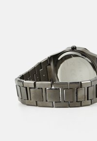 Metal watch with a matte black stainless steel band, featuring rectangular links, a round case, and a transparent back.
