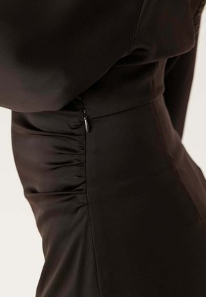 Close-up van een aansluitend zwart kledingstuk met zijplooien en een klein zichtbaar ritssluitingstrekertje in de zijnaden.