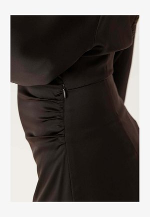 Primo piano di un capo nero aderente che mostra arricciature laterali e una piccola cerniera visibile sulla cucitura laterale.