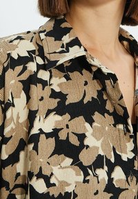 Camicia a motivi marroni e neri con colletto, caratterizzata da un tessuto testurizzato e forme floreali astratte in tutto il capo.