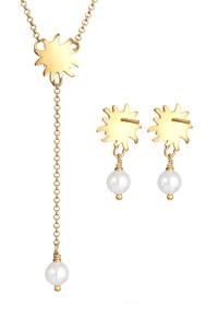 Guld smyckesset med en hängande halskedja i stiliserad solstråle-design och matchande örhängen med pärlprydnader.