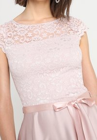 Robe en dentelle rose pâle avec manches courtes, corsage à motif floral et ruban en satin noué en un nœud à la taille.