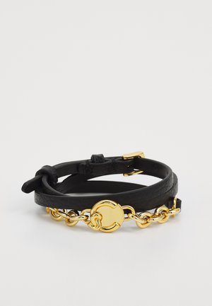 Pulseira de couro preta com um detalhe de corrente dourada e um fecho circular em ouro. O design inclui duas tiras de couro sobrepostas.
