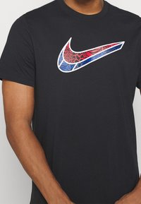 Camiseta de algodón negra con un gran logotipo colorido de Nike Swoosh, con detalles en rojo, azul y estampado animal sobre un contorno blanco.