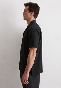 Zwarte T-shirt met korte mouwen van gestructureerde stof, met een knoopsluiting aan de voorkant en een rechte onderkant. Het heeft een ontspannen pasvorm en zijsplitsen.