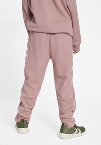 Rosa mjukisbyxor med vita sidränder, mjukt material, avslappnad passform, ihopparade med gröna träningsskor med vita detaljer.