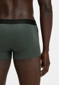 Dark green boxer shorts with a textured black waistband, showcasing a smooth fabric and fitted design on a model's lower back and thigh.