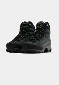 Botas de caminhada pretas com detalhes em verde e amarelo, parte superior sintética texturizada, sola Vibram e sistema de atacadores distinto. Design leve e durável.