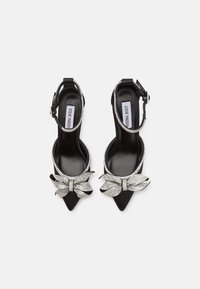 Mustat kärjetön slingback-kengät, joissa on strassikoristeltu nauha ja suuri rusetti edessä. Sileä nahkapinta.