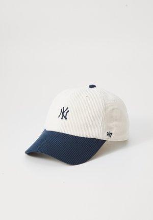 Witte corduroy baseballpet met donkerblauwe klep en geborduurd donkerblauw New York Yankees-logo aan de voorkant.