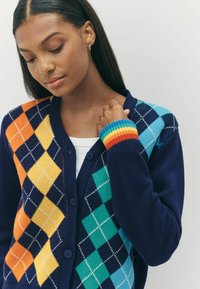 Tumedate cardigan, millel värviline argyle muster, kus on oranž, kollane, roheline ja türkiissinine, koos ribiküljega erksate vikerkaare triipudega.