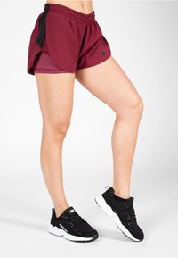 Bordeaux sportshorts met zwarte zijaccenten, elastische tailleband en binnenvoering. Gepaard met zwarte sneakers met witte zolen.