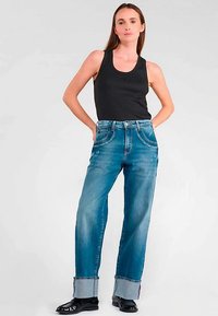 Jean en denim bleu clair avec une coupe décontractée, ourlets retroussés montrant un tissu contrastant, associé à un débardeur noir sans manches.