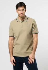 Khaki polo z granatowym kołnierzykiem i rękawami, posiadający trzy guziki przy zapięciu oraz małe logo na lewej piersi. Gładka faktura.