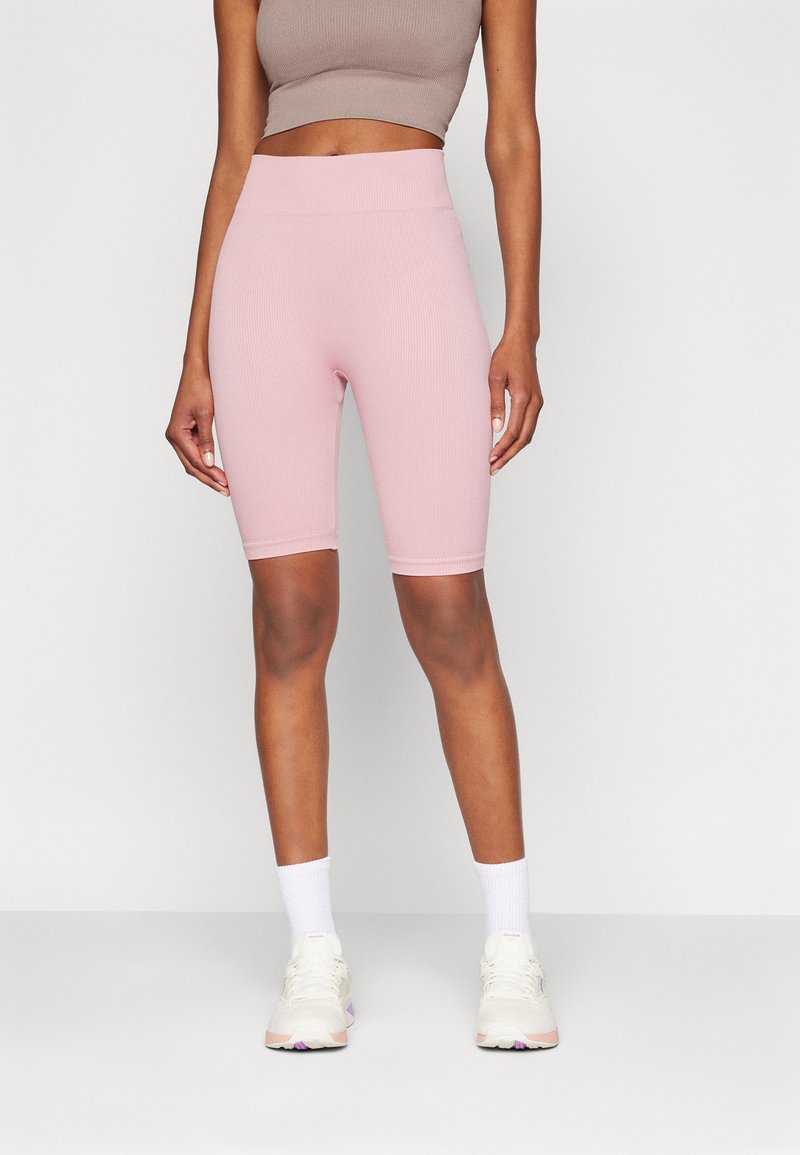 Pantaloni da bici a coste di colore rosa chiaro con vita alta, caratterizzati da una texture liscia e un design aderente. Abbinati a un top beige corto e scarpe bianche.