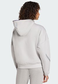 Hellgrauer Kapuzenpullover mit lässiger Passform, strukturiertem Stoff, tiefen Schultern und reflektierendem Akzent am linken Ärmel.