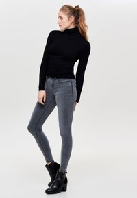 Schwarzer gerippter Rollkragenpullover kombiniert mit schmalen grauen Jeans und schwarzen Stiefeletten mit seitlichem Reißverschluss.