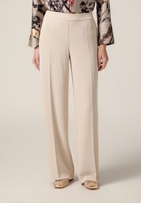 Pantaloni beige a gamba larga realizzati in tessuto morbido, con vita alta e pieghe frontali per un look sartoriale. Abbinati a scarpe di colore chiaro.