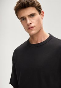 Czarny t-shirt z krótkim rękawem i klasycznym okrągłym dekoltem, wykonany z miękkiej tkaniny o gładkiej fakturze. Prosty, minimalistyczny design.