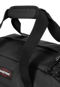 Mustaan Eastpak-reppu, jossa on kestävä kangas, kaksinkertaiset verkkohihnat, pehmustettu kahva ja vetoketjullinen lokero teksturoiduilla vetimillä.