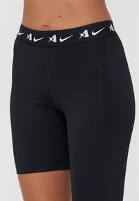 Juodos sportinės šortai su aukštu, elastingu juosmeniu, ant kurio yra balta Nike logotipo forma. Lygus, tamprus audinys.