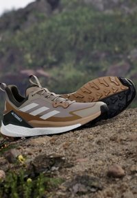 Buty do biegania w terenie Terrex w beżowym kolorze, z szarymi akcentami, teksturowaną gumową podeszwą oraz amortyzującą podeszwą pośrednią dla lepszej przyczepności i wsparcia.