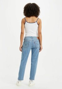 Vaqueros de mezclilla de color azul claro, con un corte relajado, bolsillos delanteros y traseros, y un parche de cuero en la cintura. Camiseta sin mangas blanca con ribete azul.