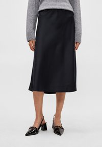 Sort satin-midi-nederdel med elastisk linning, der har en glat tekstur og en let glans, kombineret med sorte slingback-hæle.