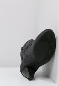Botín de ante negro con tacón bajo, cremallera lateral y suela de goma texturizada. El interior es sin adornos y la forma es estilizada.