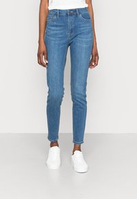 Modré džíny s vysokým pasem a slim fit, se pěti kapsami, jemnými švy a zkrácenou délkou ke kotníkům. Nosí se s bílými teniskami.